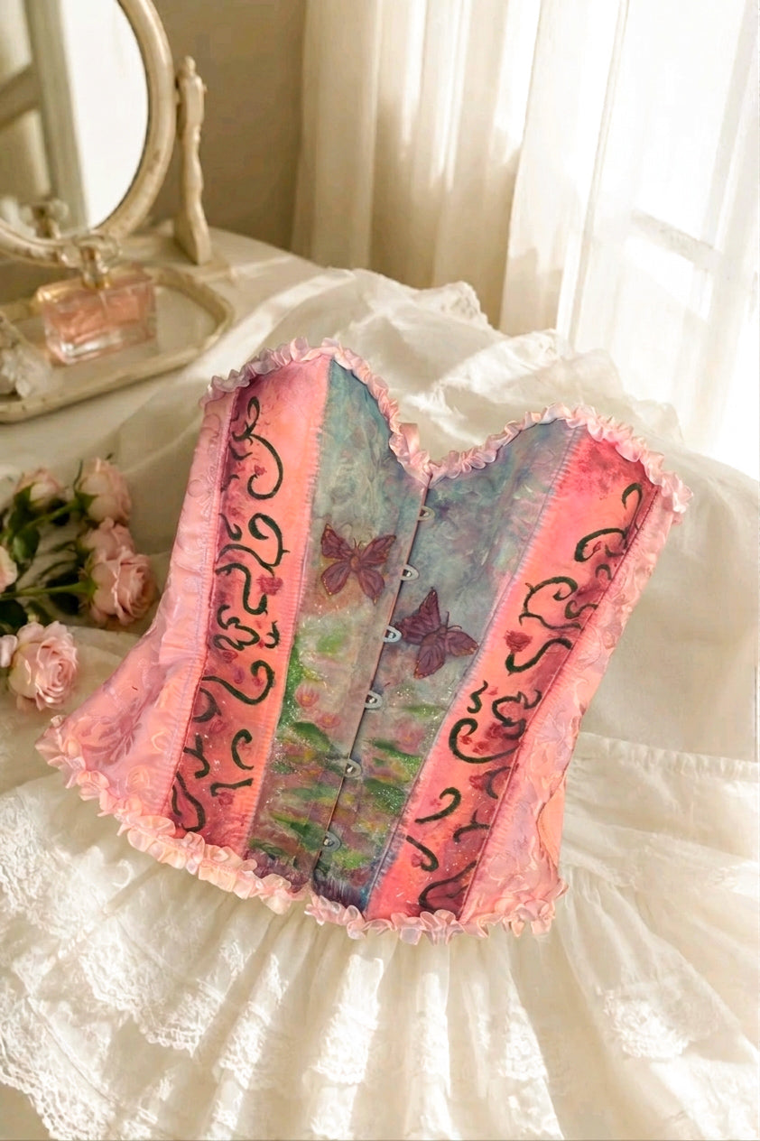 Pink and blue corset top by Closet Albita. Features include a front busk closure, pink ruffle trim, and a hand-painted meadow scene with purple butterflies.