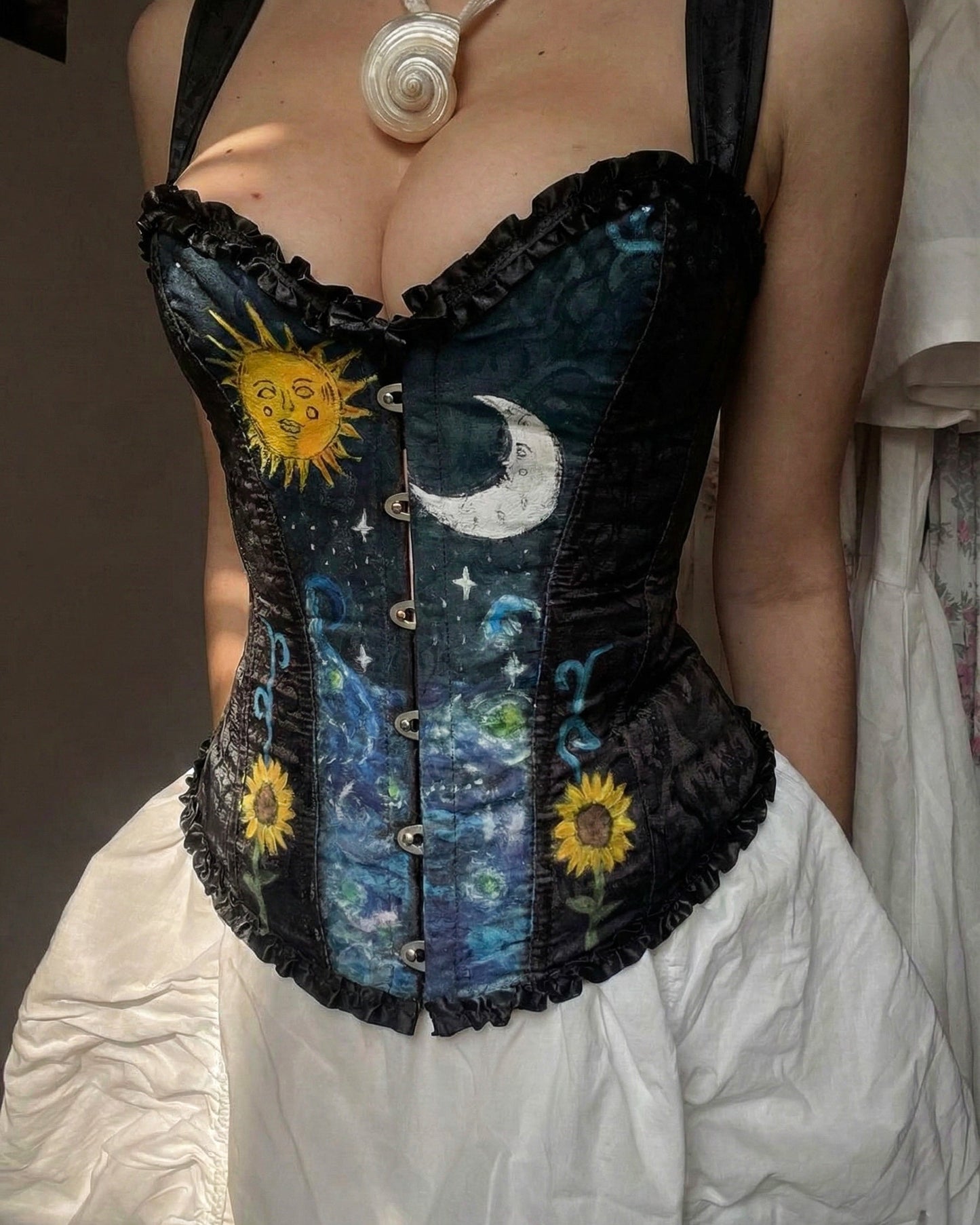 Front view of a model wearing a hand-painted black celestial corset by Closet Albita, featuring a sun, moon, stars, and sunflowers with black ruffle trim.